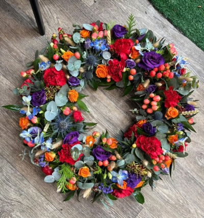 Autumnal Theme Wreath Tribute - We will create a wreath arrangement using a beautiful mix of reds, oranges, purples and blues. Exact flowers used may vary depending on availability but theme will remain the same. 

Standard 12"
Medium 14"
Large 16"